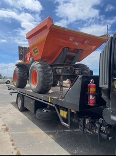An orange dumper loaded on the back of the tilt tray truck